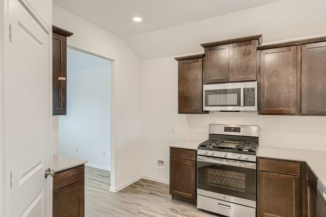 Kitchen featuring stainless steel appliances, dark brown cabinets, light countertops, light wood-style flooring, and vaulted ceiling | Image 8