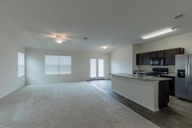 Kitchen with stainless steel fridge with ice dispenser, black microwave, gas range, baseboards, and open floor plan | Image 5