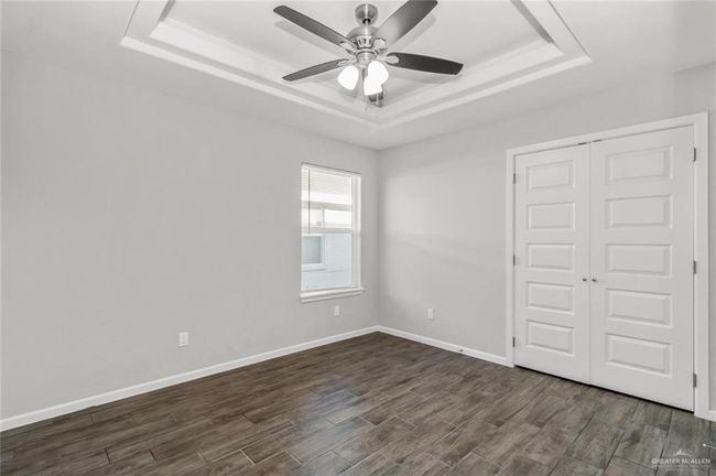 Unfurnished bedroom with a tray ceiling, dark wood-style floors, a closet, baseboards, and a ceiling fan | Image 6