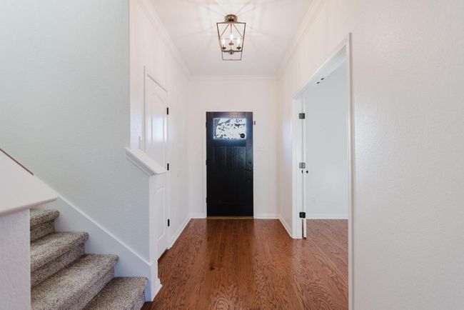 Entrance foyer with a notable chandelier, ornamental molding, wood finished floors, baseboards, and stairs | Image 4