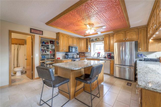 Kitchen with appliances with stainless steel finishes, brown cabinetry, light stone countertops, and a center island | Image 13