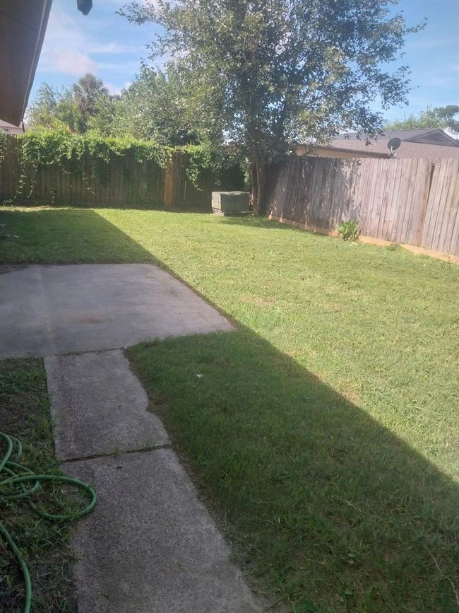 This photo shows a single-story brick house with a gabled roof. The front yard features a grassy lawn and walkway leading to the entrance. There are a few mature trees and fenced back yard. The house has a simple, inviting exterior. | Image 44