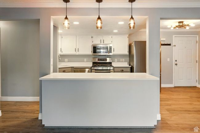 Kitchen with stainless steel appliances, crown molding, baseboards, white cabinetry, and light wood-style floors | Image 7