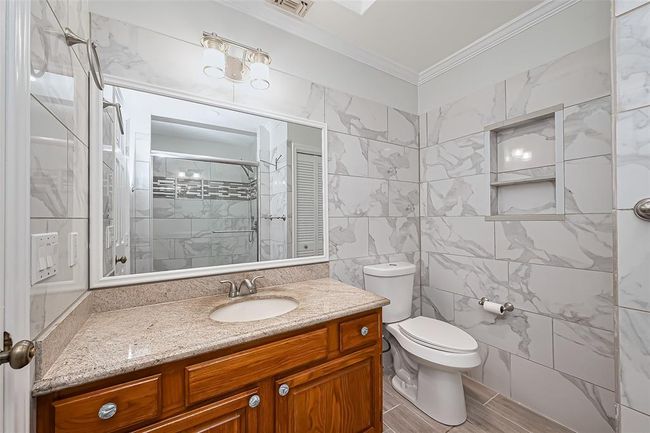 Upstairs bathroom features elegant marble-patterned tile walls, a granite countertop with a wooden vanity, and a large mirror. It includes a new toilet and a shower with stylish tile accents, providing a sleek and functional space. | Image 17