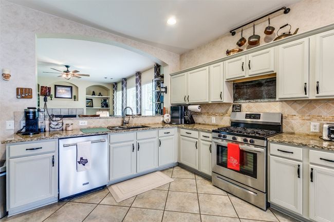 Kitchen with stainless steel appliances, a sink, backsplash, arched walkways, and light stone counters | Image 7