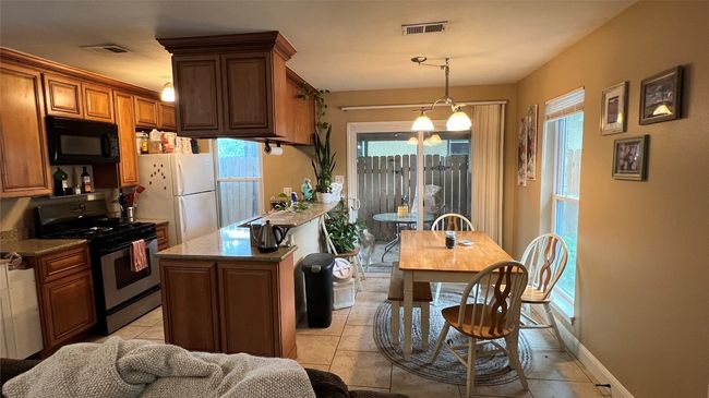 Kitchen with stainless steel gas range oven, black microwave, freestanding refrigerator, a peninsula, and brown cabinets | Image 15