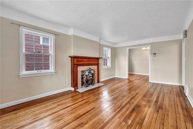 Unfurnished living room featuring wood-type flooring, baseboards, a fireplace, a textured ceiling, and a notable chandelier | Image 26