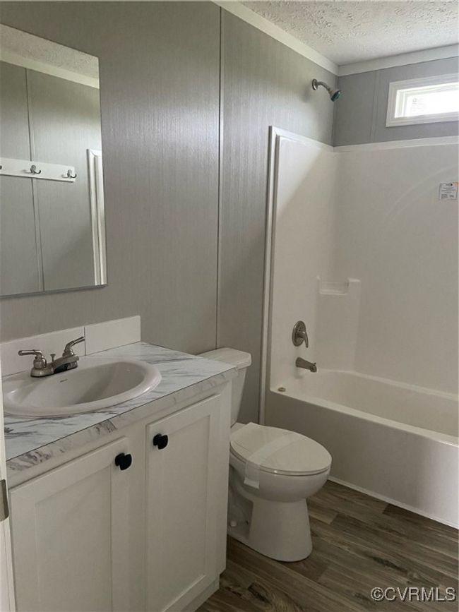 Full bathroom featuring a textured ceiling, vanity, shower / washtub combination, toilet, and hardwood / wood-style flooring | Image 6