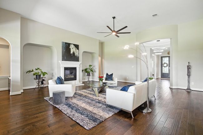 Living room featuring hardwood / wood-style flooring, ceiling fan, a glass covered fireplace, and arched walkways | Image 7
