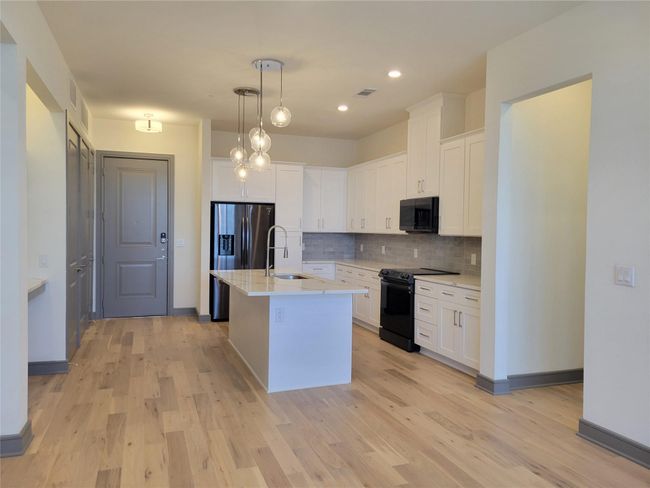 Kitchen with black appliances, hanging light fixtures, an island with sink, white cabinets, and backsplash | Image 9