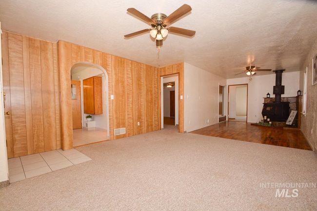 Unfurnished living room featuring a ceiling fan, a wood stove, carpet, arched walkways, and a textured ceiling | Image 17