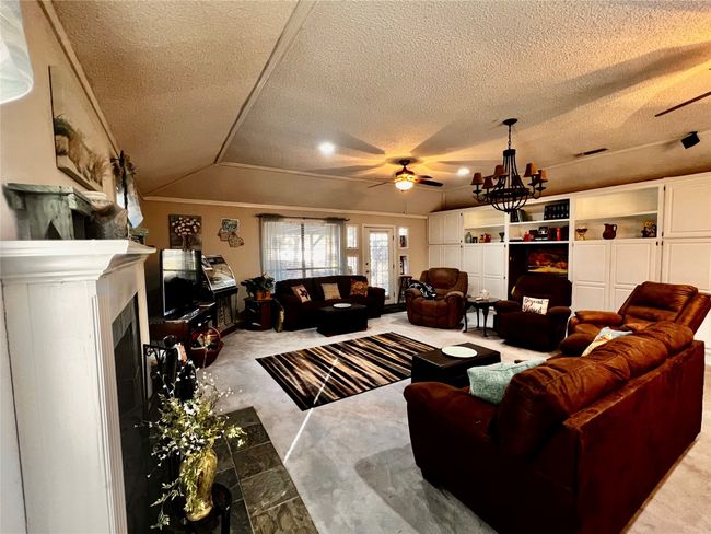 Living room with ceiling fan with notable chandelier, a textured ceiling, carpet floors, and lofted ceiling | Image 16