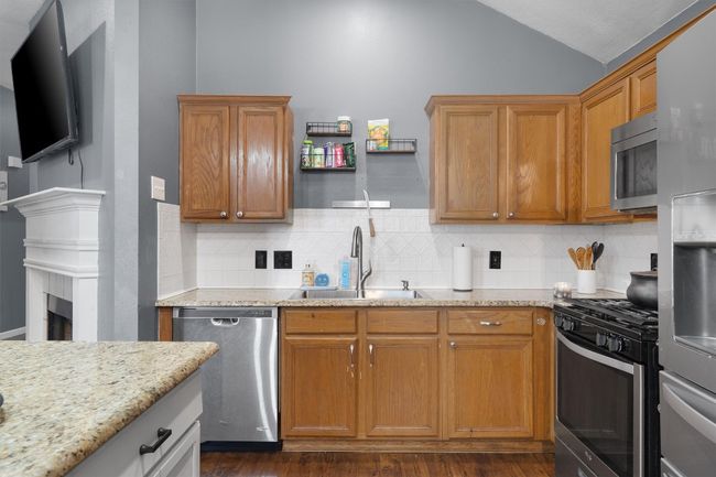 Kitchen with stainless steel appliances, a sink, backsplash, lofted ceiling, and light stone countertops | Image 8