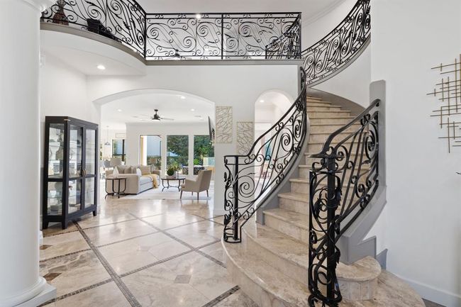View of the open entryway, where the grand staircase leads into the expansive living room. Walls of windows fill the space with natural light, creating a bright and airy atmosphere. | Image 7