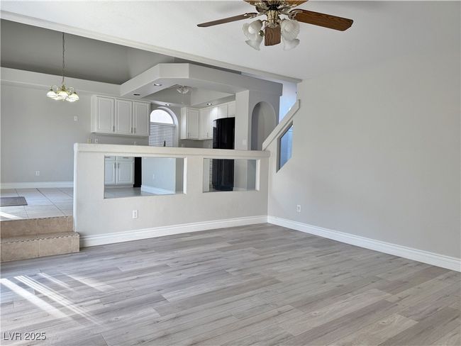 Unfurnished living room with light wood-type flooring, arched walkways, baseboards, and ceiling fan with notable chandelier | Image 21