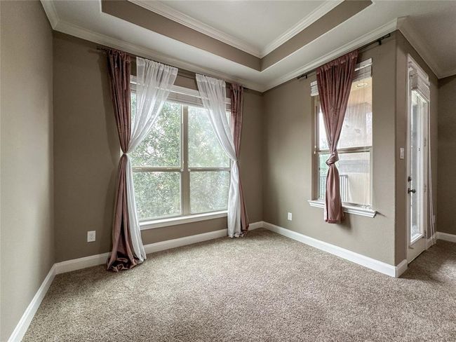 Bright room with large windows, neutral walls, and carpeted floors. Features a tray ceiling and elegant drapery, creating a cozy atmosphere. | Image 26