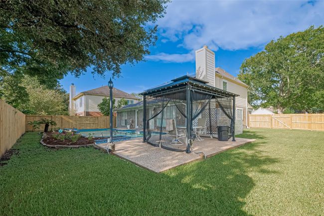 Backyard oasis features a saltwater pool and hot tub, all surrounded by a brand-new perimeter fence. Enjoy outdoor living under the pergola, with plenty of space to relax or entertain. Robotic pool cleaners are included for easy maintenance. Spacious yard extends to the side, perfect for play or gardening. | Image 39