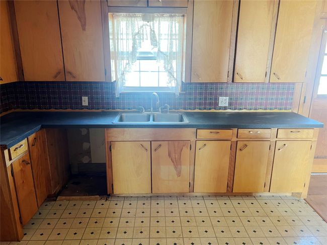 Kitchen featuring decorative backsplash, a sink, dark countertops, and light floors | Image 7