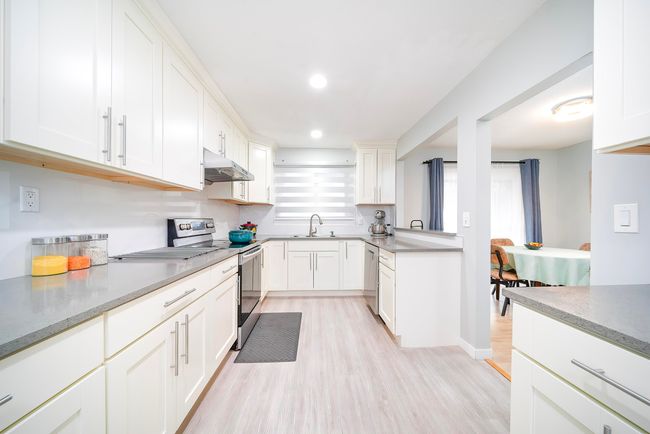 Kitchen featuring white cabinetry, stainless steel appliances, under cabinet range hood, a sink, and light wood finished floors | Image 22