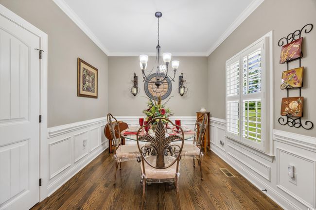 Dining area with a chandelier, dark wood finished floors, crown molding, wainscoting, and a decorative wall | Image 10