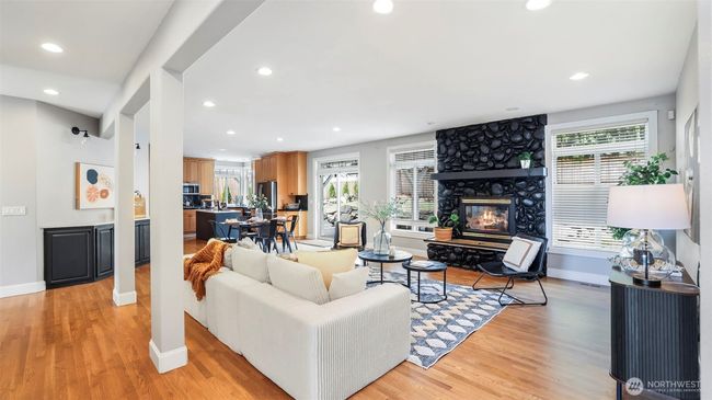 This vast open-concept space combines the living room, kitchen, dining area, and a charming nook—highlighted by warm wood flooring and a bold, stone-accented feature fireplace that adds character and charm | Image 15