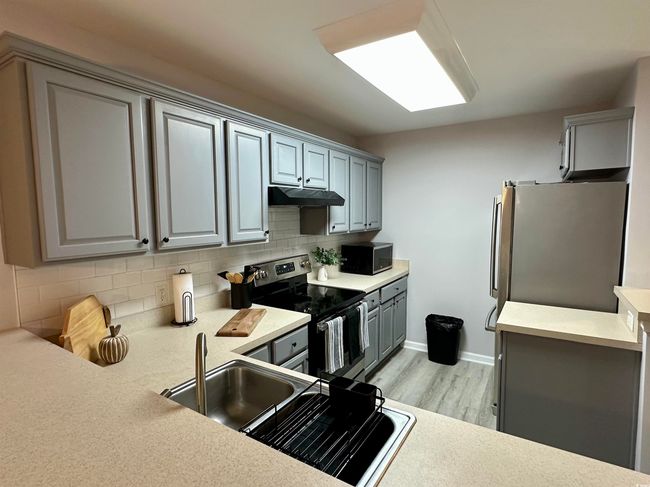 Kitchen featuring baseboards, an inviting chandelier, a peninsula, freestanding refrigerator, and light wood-style floors | Image 11