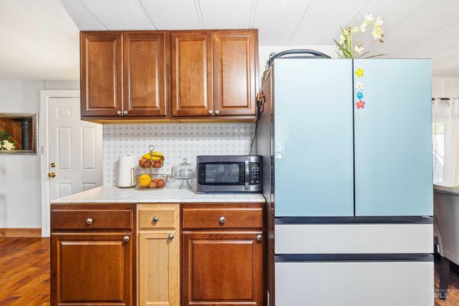 Kitchen featuring freestanding refrigerator, stainless steel microwave, wood finished floors, decorative backsplash, and tile counters | Image 9