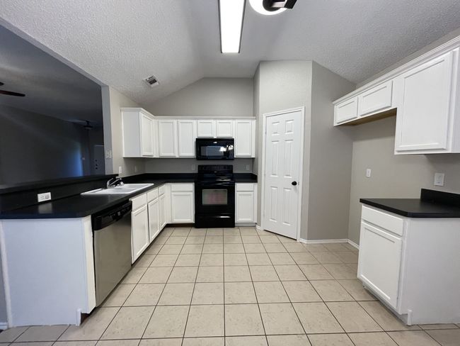Kitchen with black appliances, dark countertops, light tile patterned flooring, vaulted ceiling, and white cabinetry | Image 4