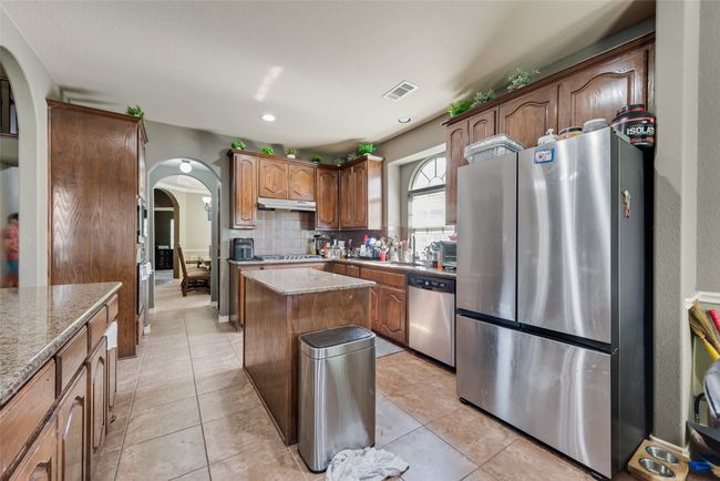 Kitchen featuring stainless steel appliances, arched walkways, decorative backsplash, a kitchen island, and light stone countertops | Image 11