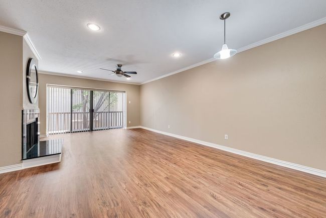 Unfurnished living room featuring crown molding, light wood-style flooring, a ceiling fan, a fireplace with raised hearth, and baseboards | Image 10