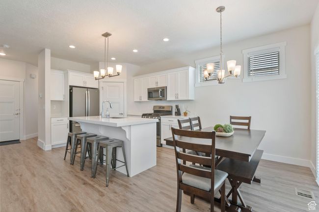 Kitchen with stainless steel appliances, a chandelier, a kitchen breakfast bar, light countertops, and light wood-style flooring | Image 5