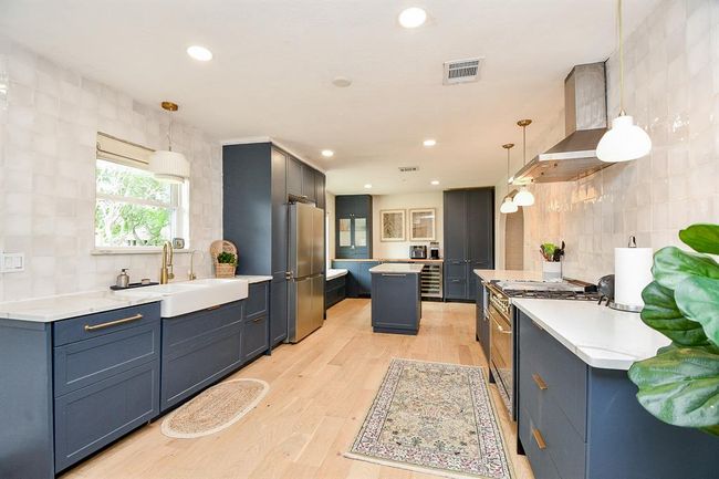 Bright, modern kitchen with navy cabinets, stainless steel appliances, and light wood flooring. Features a farmhouse sink, ample counter space, and stylish pendant lighting. | Image 21