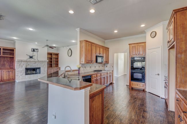 Kitchen featuring a fireplace, black appliances, kitchen peninsula, sink, and a breakfast bar area | Image 23