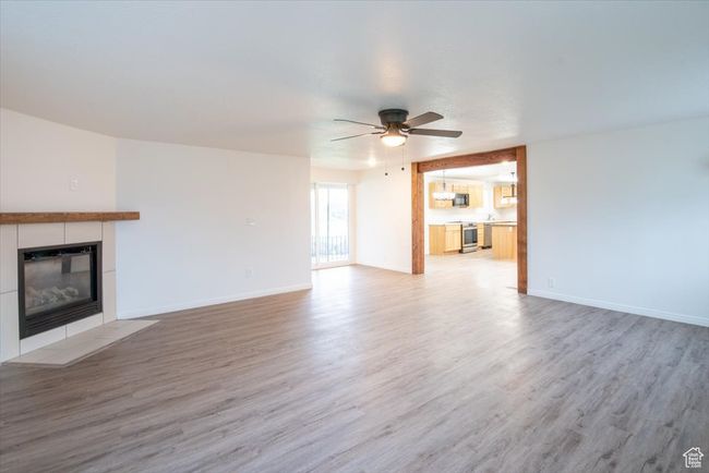 Unfurnished living room featuring a tiled fireplace, baseboards, a ceiling fan, and light wood-style flooring | Image 18