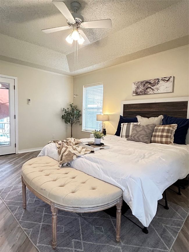 Bedroom featuring a raised ceiling, a textured ceiling, wood finished floors, baseboards, and ceiling fan | Image 34