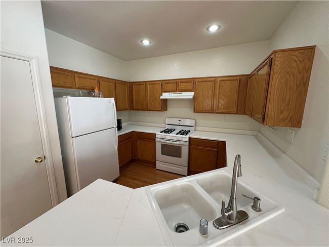 Kitchen with white appliances, under cabinet range hood, a sink, brown cabinetry, and light countertops | Image 14