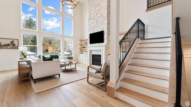 Living area with stairway, a chandelier, a large fireplace, a towering ceiling, and light wood-style flooring | Image 17