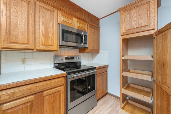 Kitchen featuring stainless steel appliances, decorative backsplash, light countertops, crown molding, and light wood-type flooring | Image 19