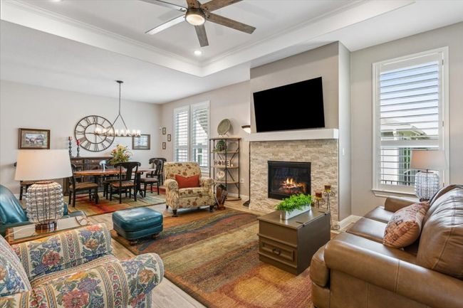 Great Room area open to Dining Room with an upgraded ceiling fan, a chandelier, recessed lighting, crown molding, and a stone fireplace | Image 10