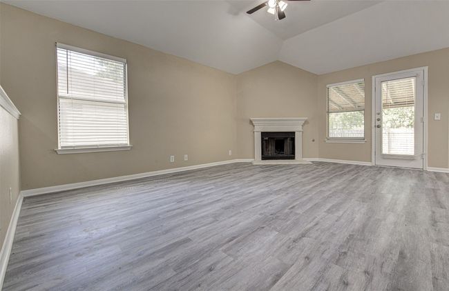 Unfurnished living room featuring a ceiling fan, wood finished floors, a fireplace with raised hearth, and lofted ceiling | Image 4