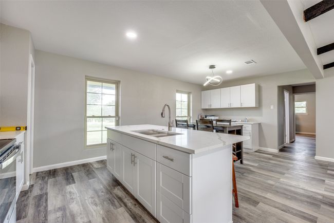Kitchen with a chandelier, light wood-type flooring, white cabinetry, a center island with sink, and recessed lighting | Image 14