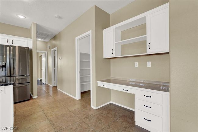 Kitchen with stainless steel fridge, built in desk, white cabinets, open shelves, and tile patterned floors | Image 12
