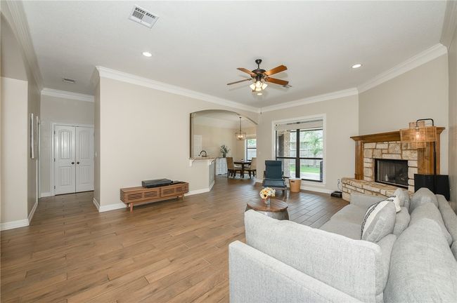 Living room featuring arched walkways, light wood-style flooring, ornamental molding, a stone fireplace, and visible vents | Image 7