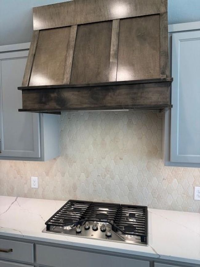 Kitchen with gray cabinets, light stone counters, decorative backsplash, wall chimney range hood, and stovetop | Image 12