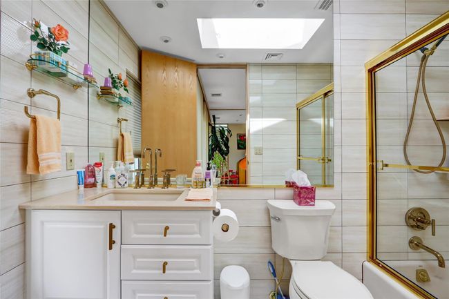 Full bathroom featuring tile walls, a skylight, toilet, and enclosed tub / shower combo | Image 21