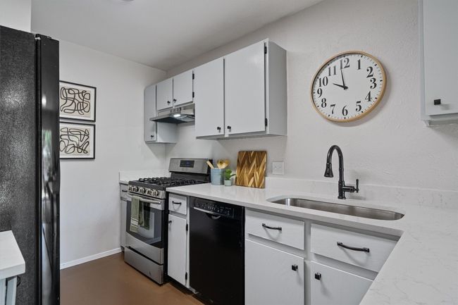Kitchen featuring black appliances, under cabinet range hood, light countertops, white cabinetry, and concrete flooring | Image 9