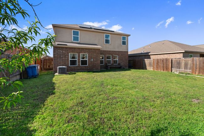 Rear view of house with central AC, a lawn, a fenced backyard, roof mounted solar panels, and brick siding | Image 33