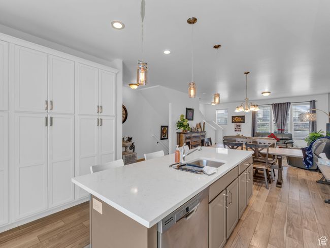 Kitchen with stainless steel dishwasher, a chandelier, open floor plan, an island with sink, and light wood finished floors | Image 11