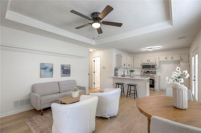 Living room with a textured ceiling, a raised ceiling, light wood-style floors, a ceiling fan, and ornamental molding | Image 4