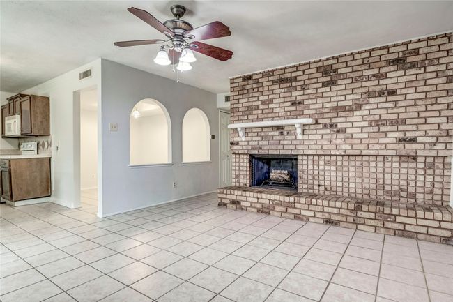 Unfurnished living room with a brick fireplace, a ceiling fan, light tile patterned floors, and baseboards | Image 19